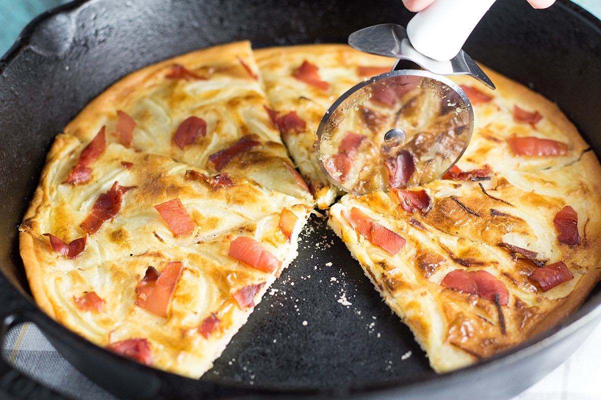 Tarte Flambee or Flammkuchen is a savory Alsatian pizza, topped with delicious sauce, onion and bacon! | cookingtheglobe.com