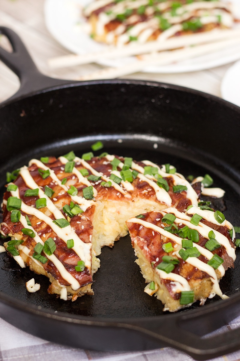 This traditional Japanese pancake (Okonomiyaki) is filled with cabbage and topped with sliced pork and amazing sauce! | cookingtheglobe.com
