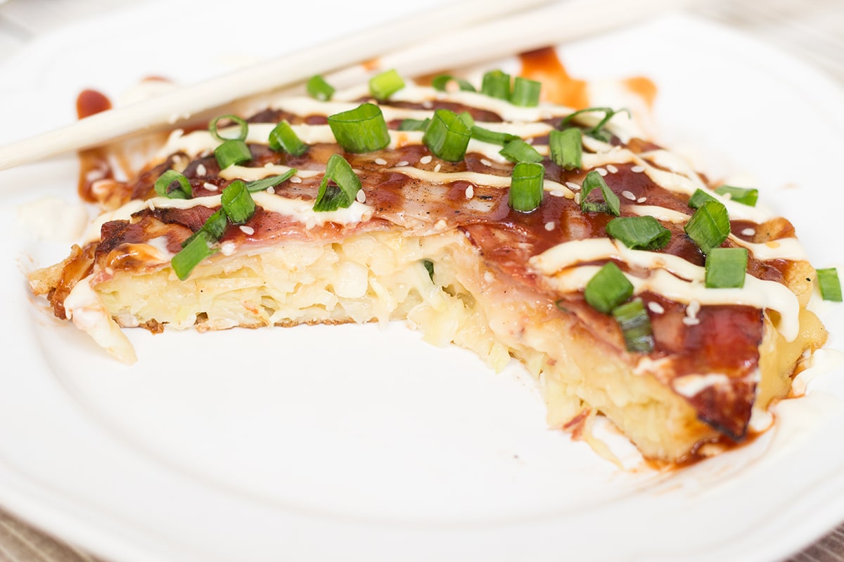 This traditional Japanese pancake (Okonomiyaki) is filled with cabbage and topped with sliced pork and amazing sauce! | cookingtheglobe.com