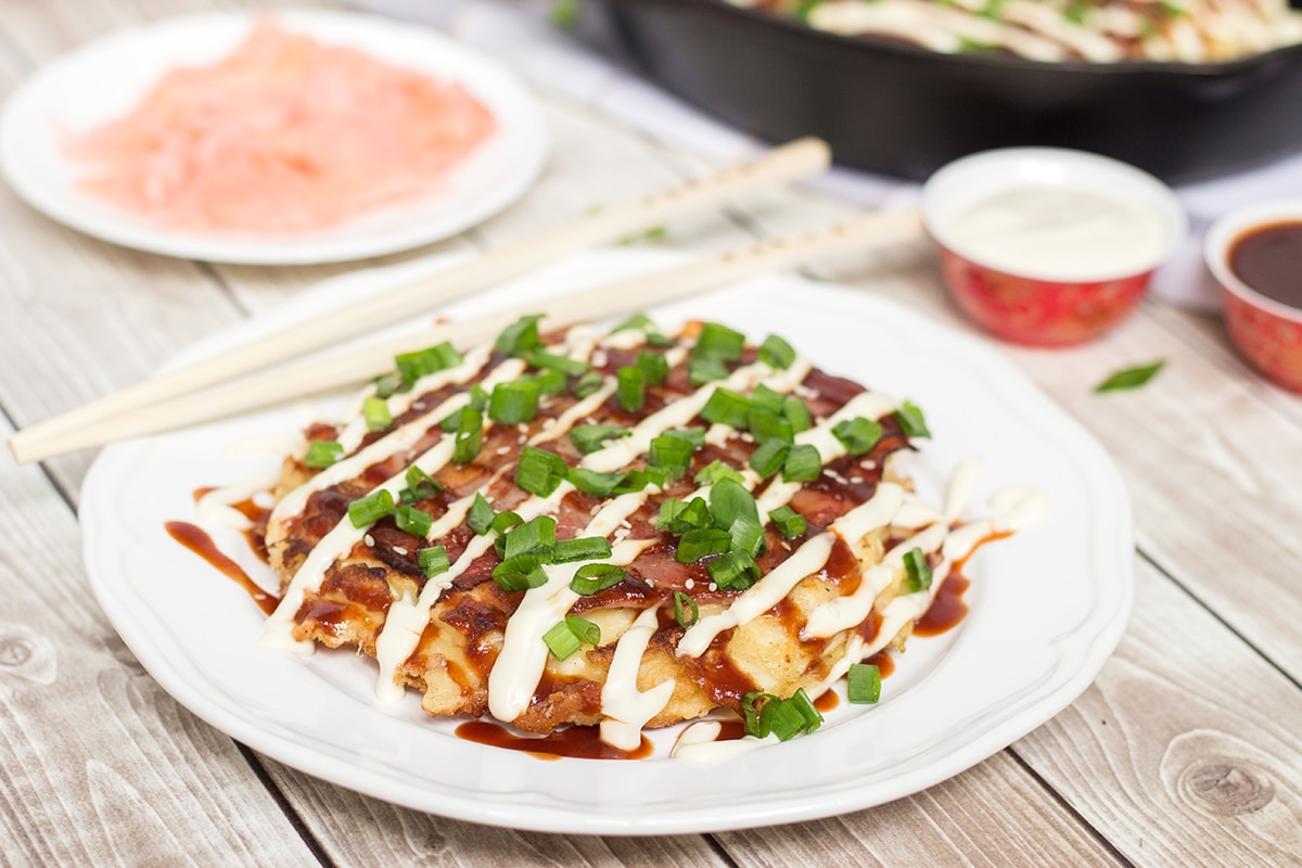 These traditional Japanese pancakes (Okonomiyaki) are filled with cabbage and topped with sliced pork and amazing sauce! | cookingtheglobe.com