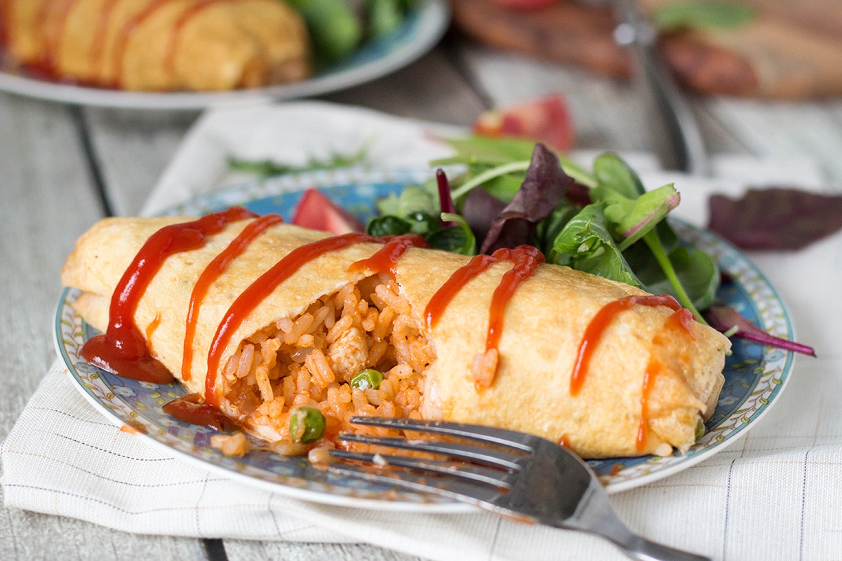 Omurice is a Japanese dish which got its name from a combo of words "omelette" and "rice". Basically, it's ketchup flavored rice cooked with chicken, peas, and wrapped in a thin crepe-like omelette. Pure heaven! | cookingtheglobe.com