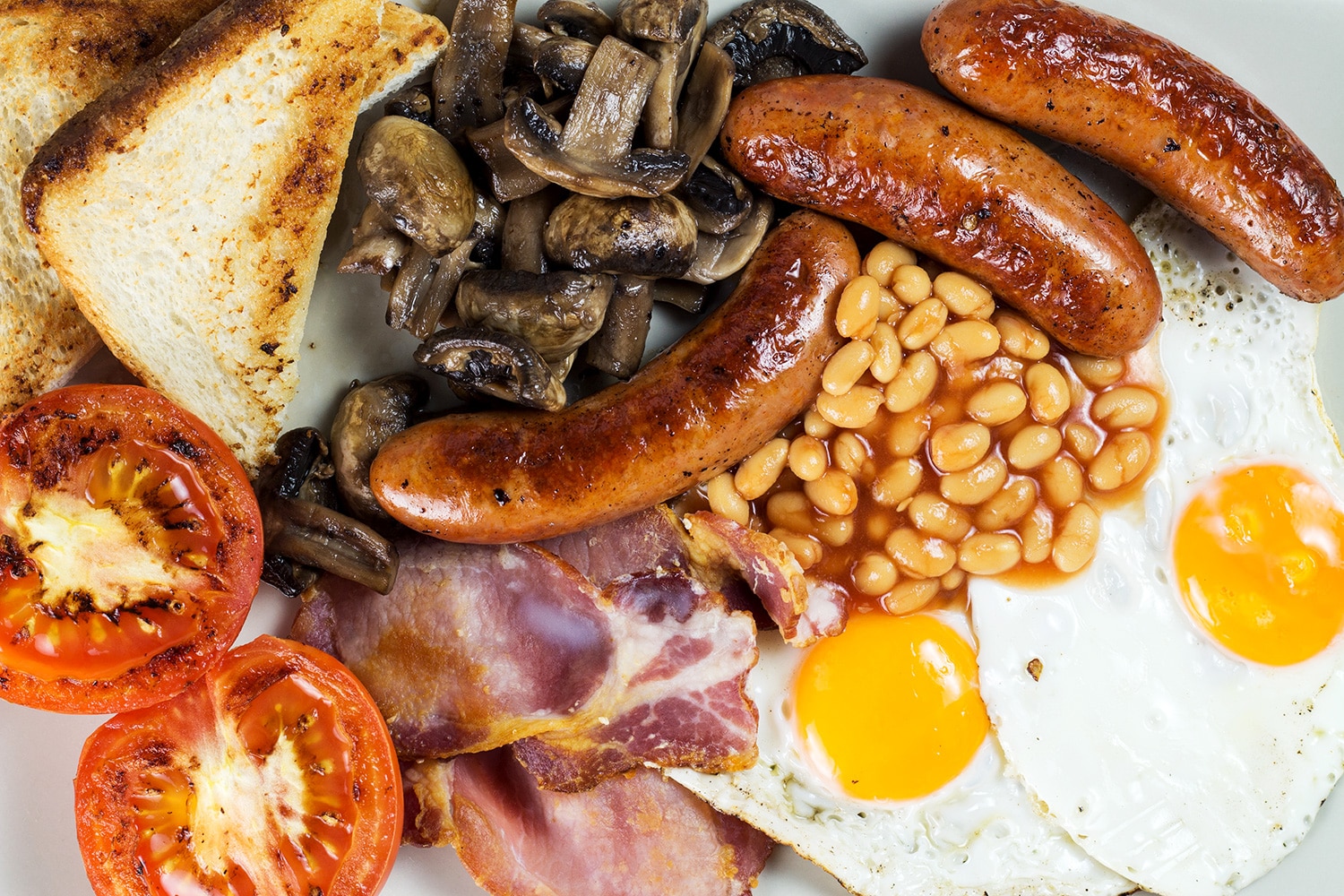 A look at the most iconic morning fare in the world - English breakfast. This hearty meal features eggs, sausages, bacon, beans, mushrooms, and more! | cookingtheglobe.com