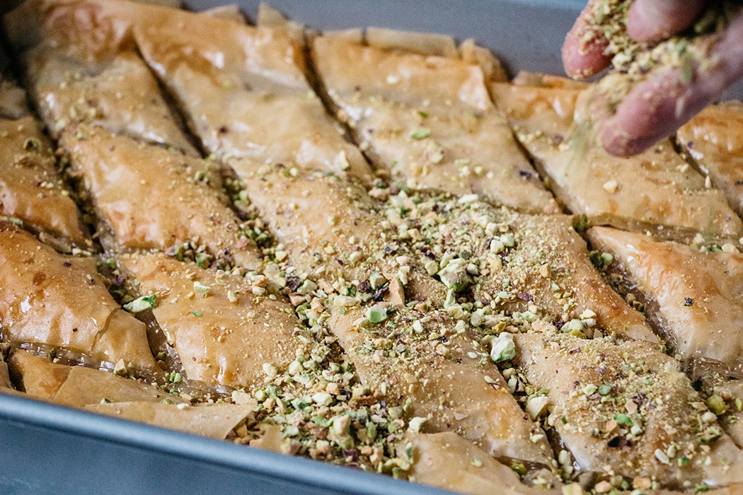 Sprinkling pistachios over baked Turkish Baklava right before serving