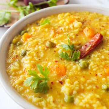 White bowl of rice and lentils on table next to fresh vegetables