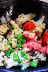 Tomatoes and green peas on top of cauliflower in skillet