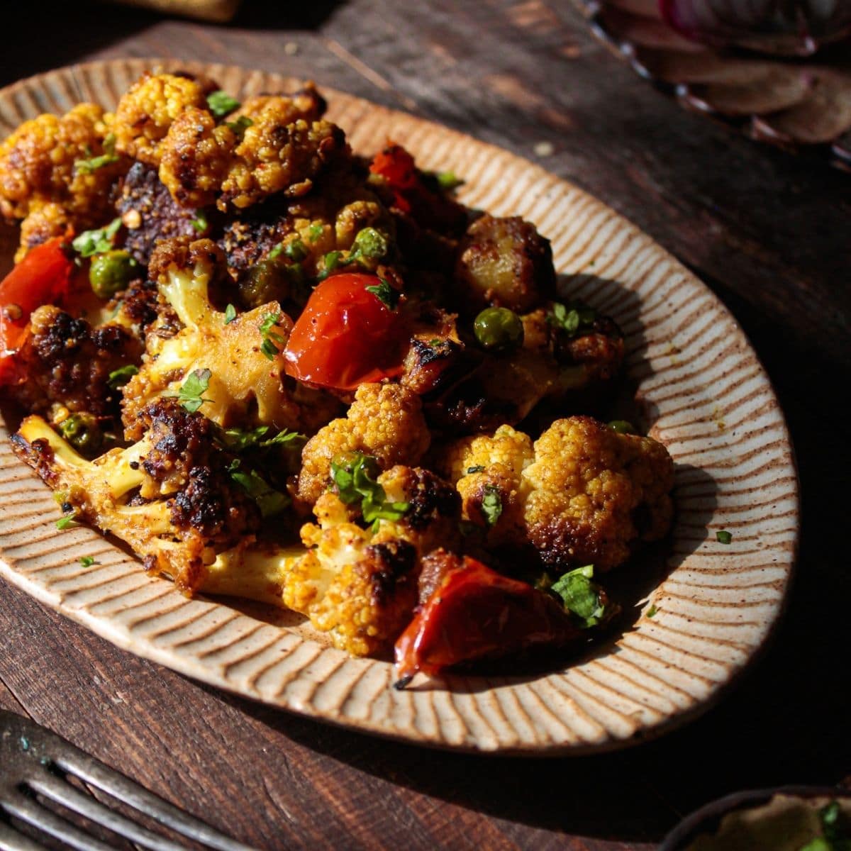 Tan platter with potato curry stir fry sitting on table by fork