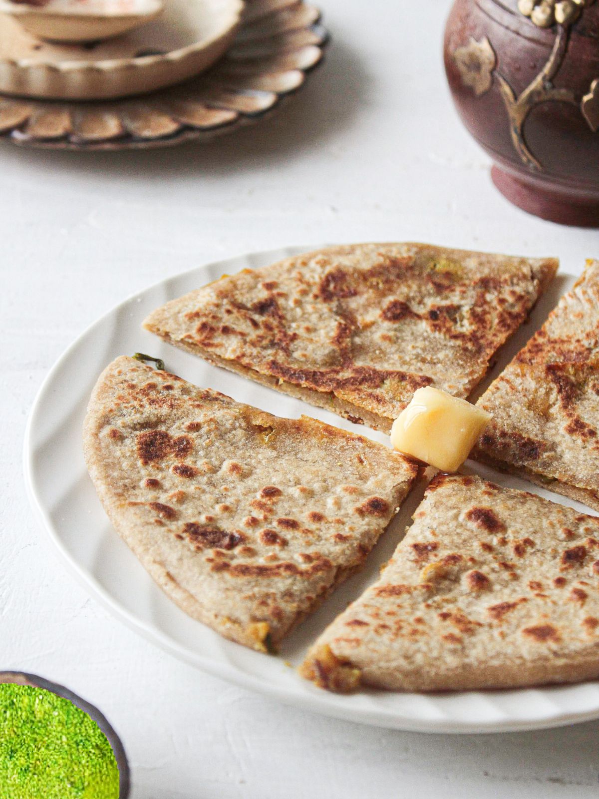 Aloo paratha on white plate cut into 4 triangles with butter on top