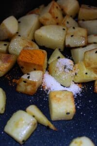 Potato chunks in skillet with turmeric and salt