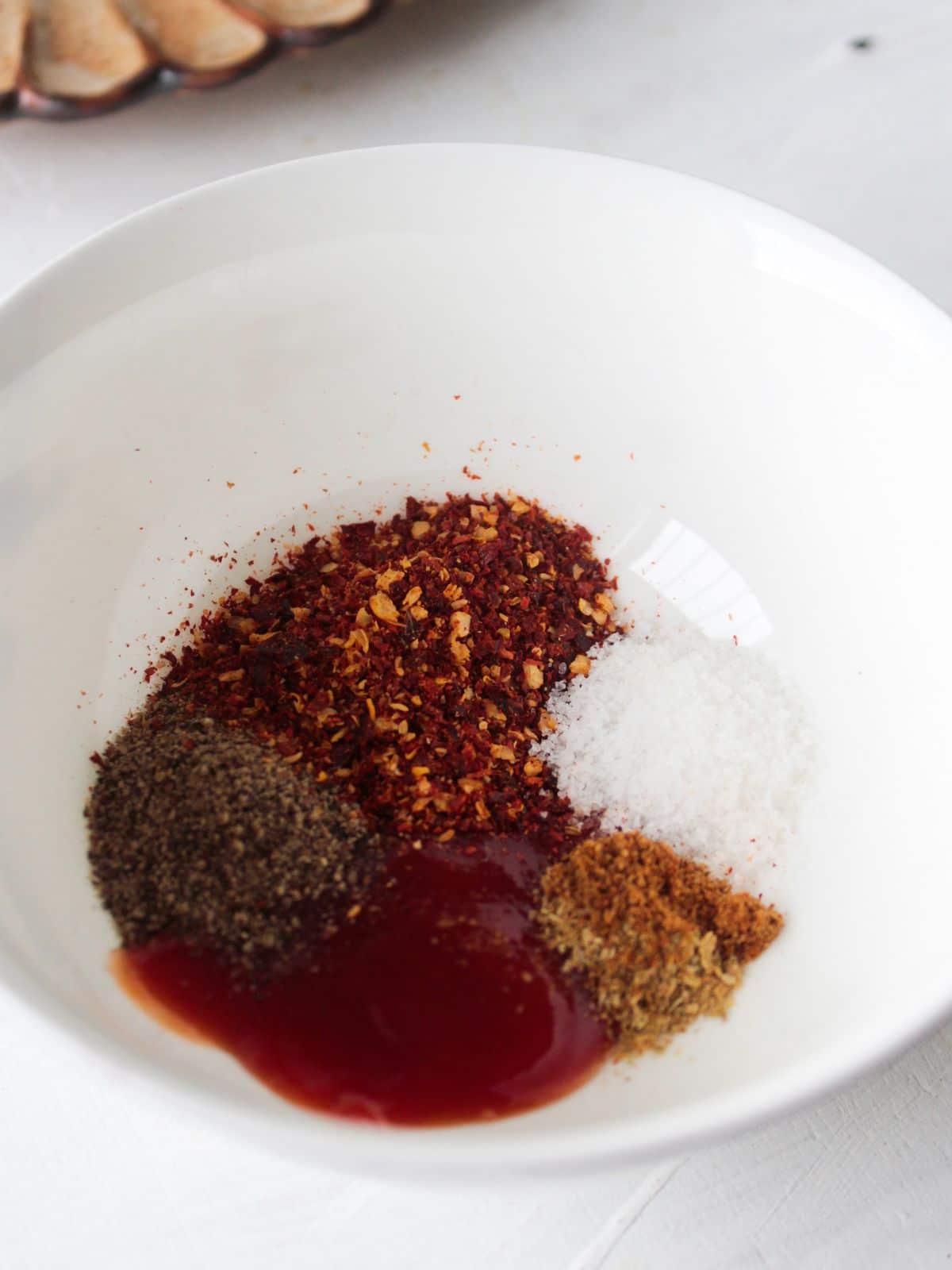 White bowl with 4 spices and a dark red liquid for marinating chicken