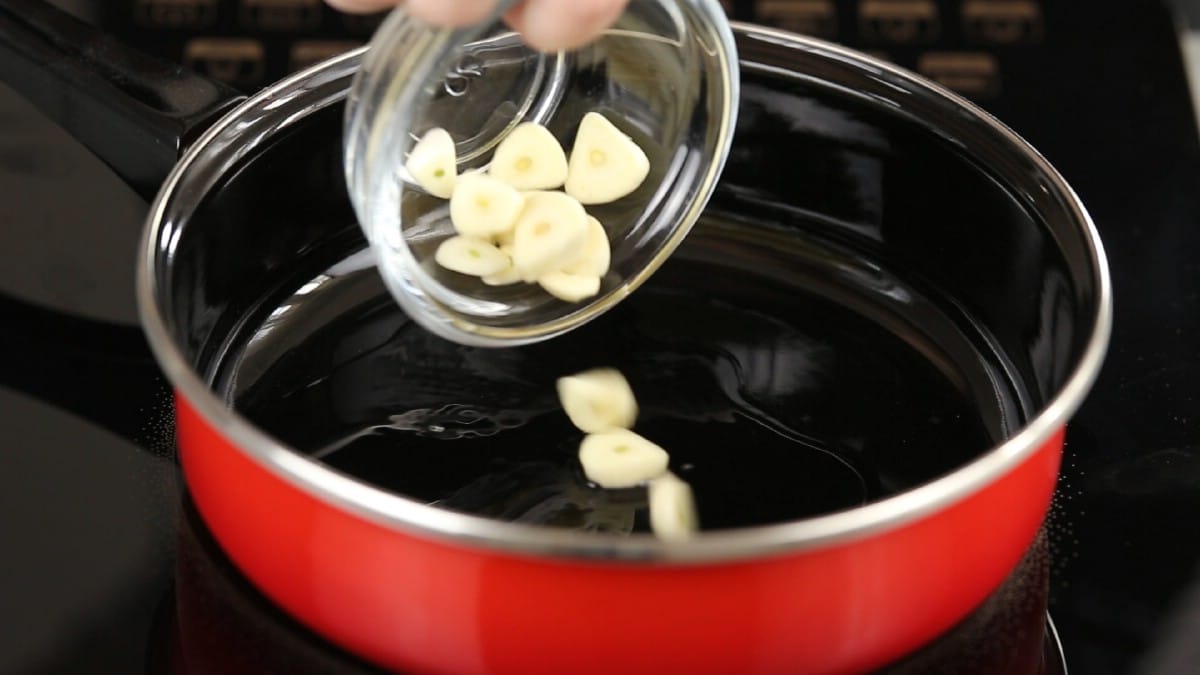 Glass bowl of garlic slices being poured into red skillet