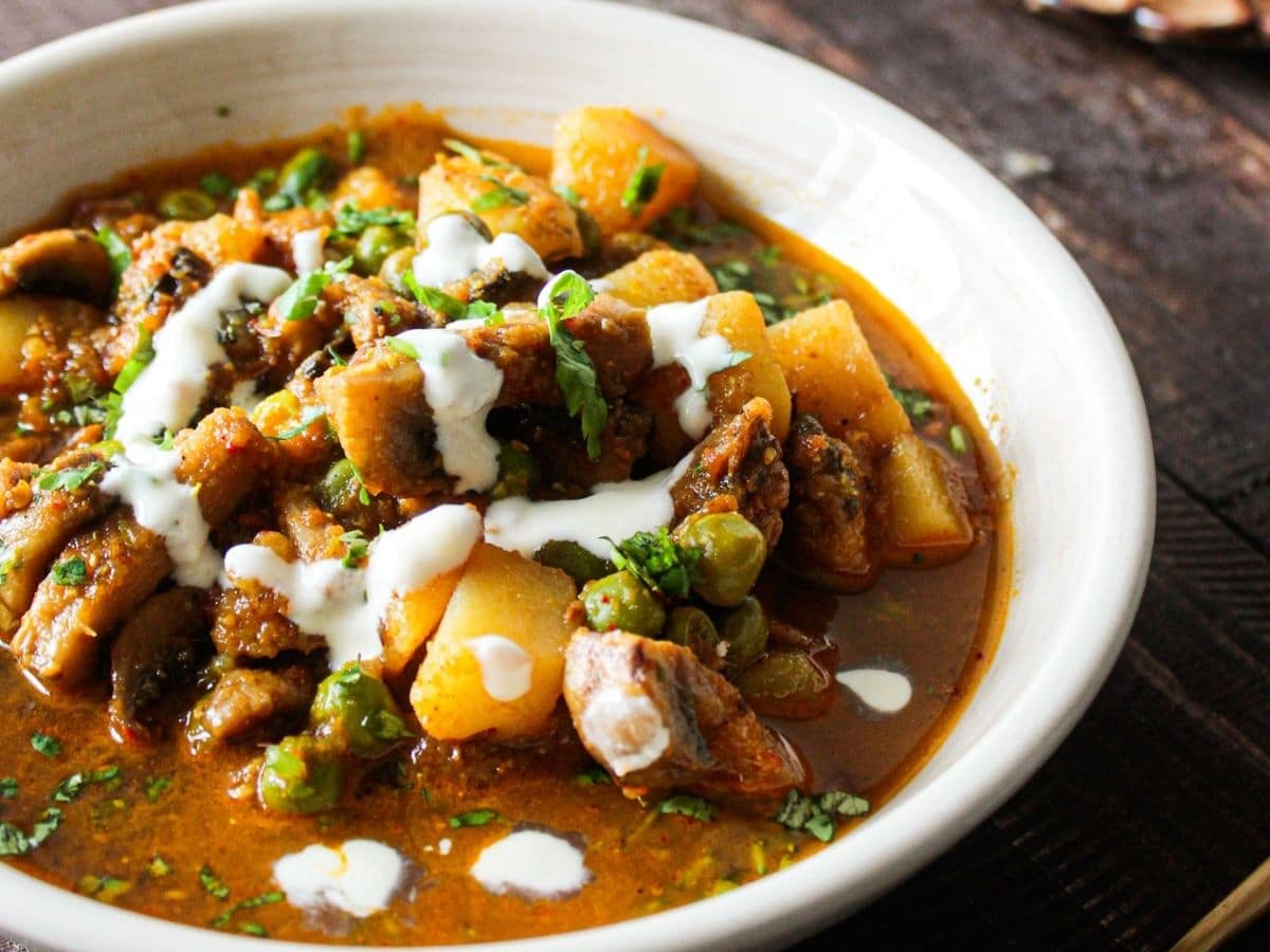 White bowl filled with curry including mushrooms and potatoes topped with cream and cilantro