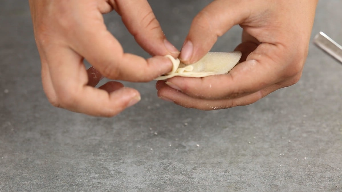Hand folding dumpling wrapper over filling