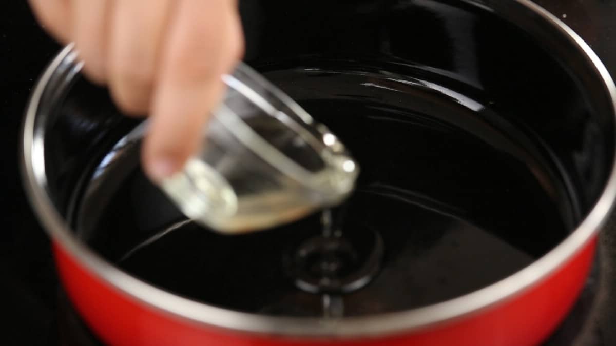 Hand pouring oil into red skillet