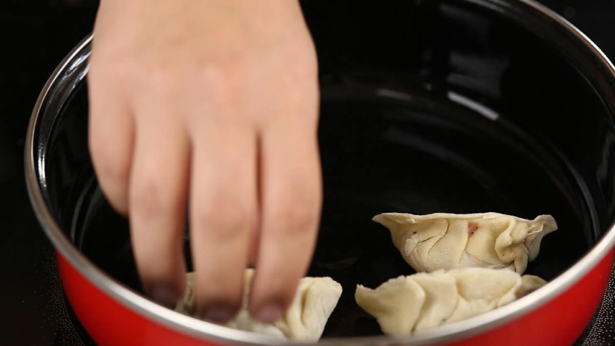 Hand placing dumplings into red skillet