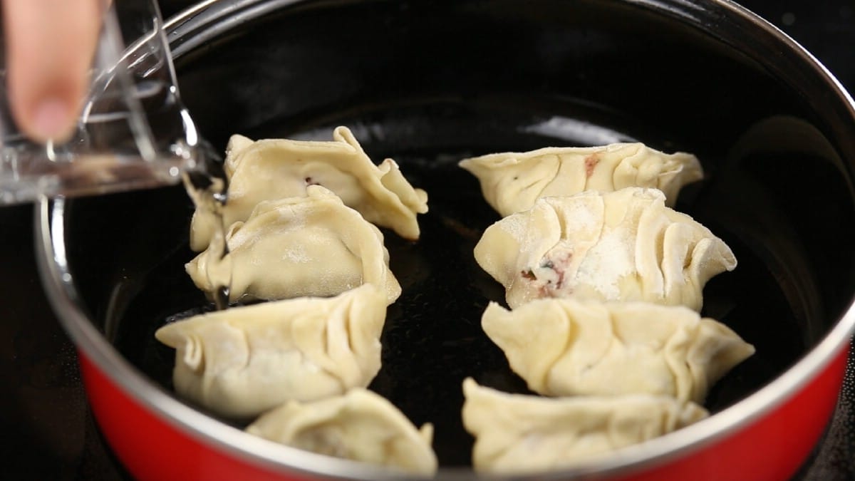 Dumplings in red and black skillet with hand pouring water in side