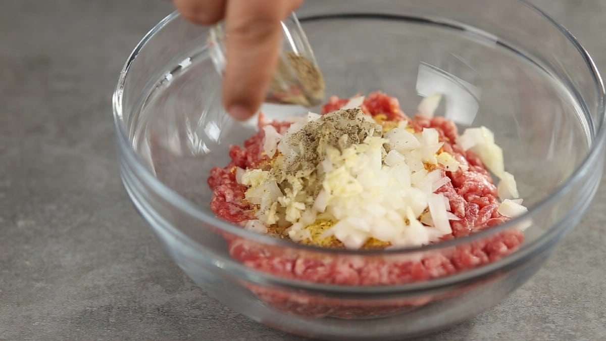 Seasoning being added to glass bowl of meat