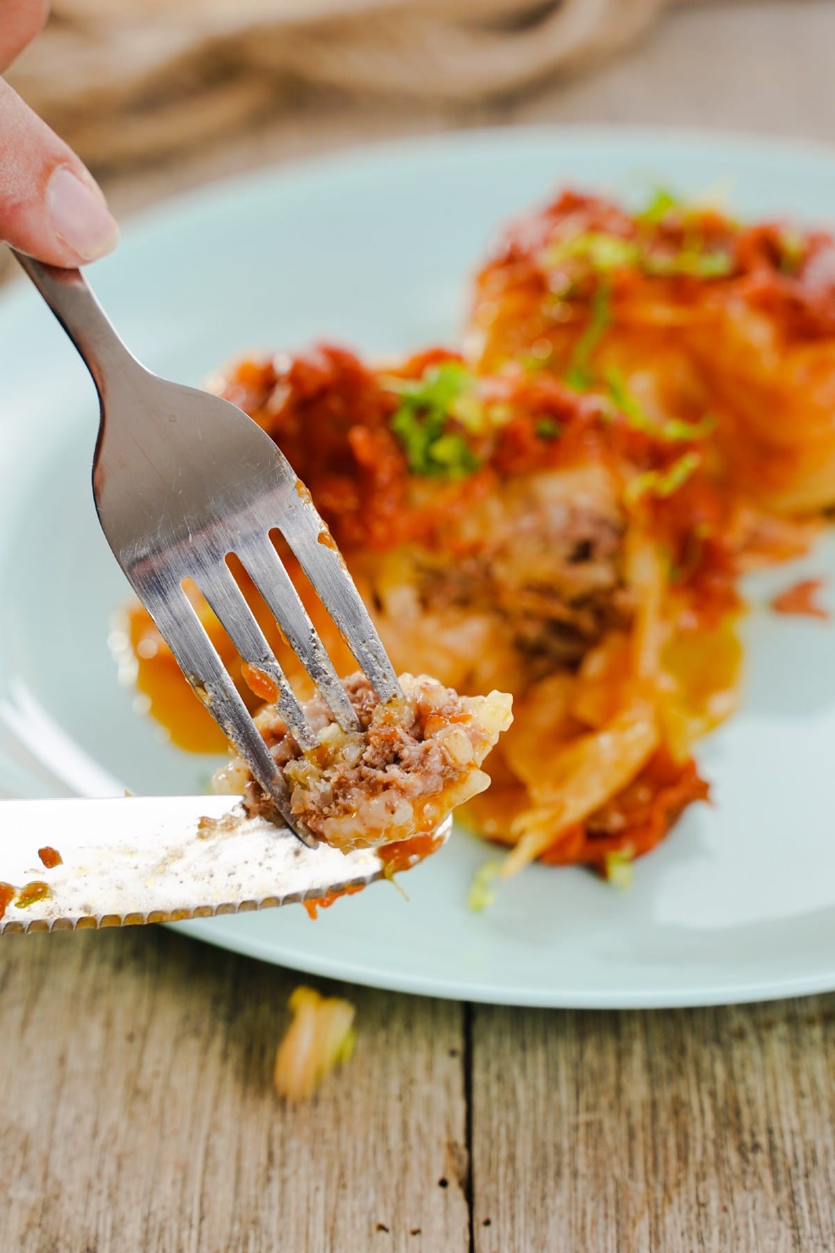 Plate of stuffed cabbage rolls with fork and knife holding bite over the top
