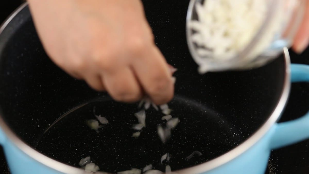 Hand adding onion to bottom of saucepan