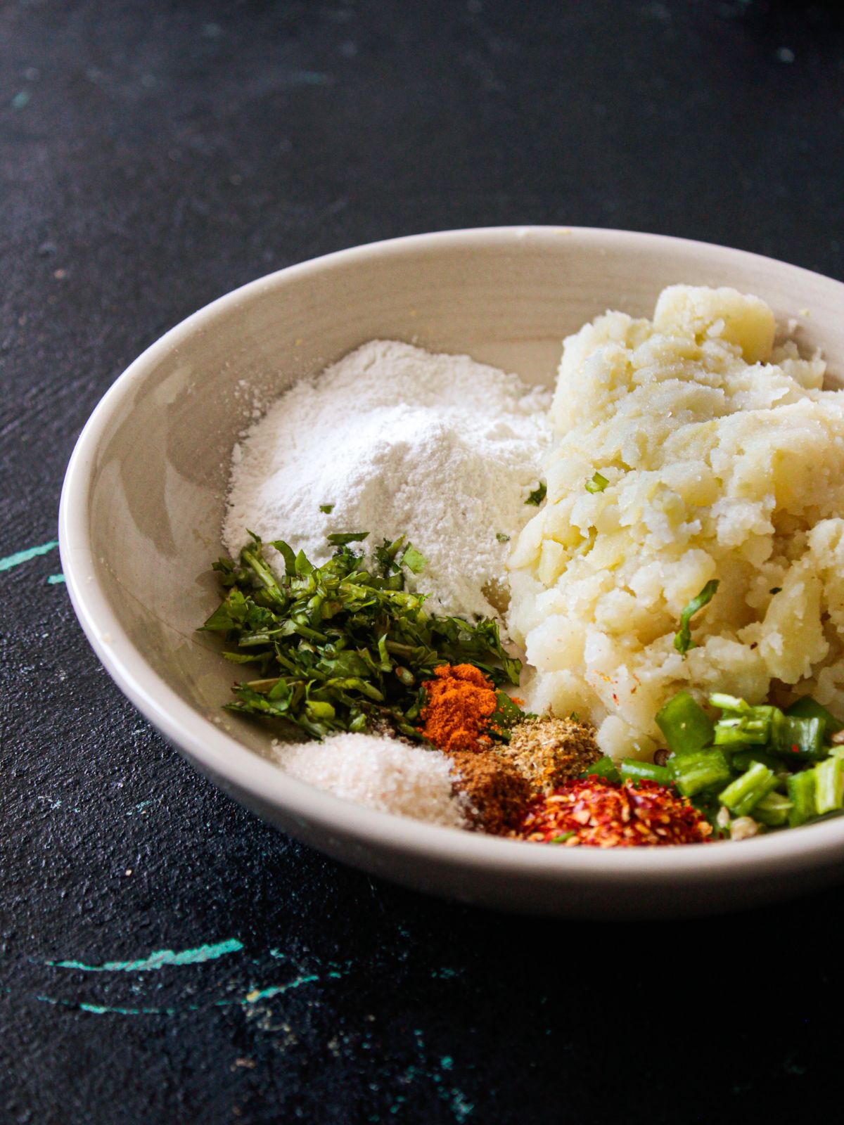 Large white bowl filled with potatoes and spices on a black table