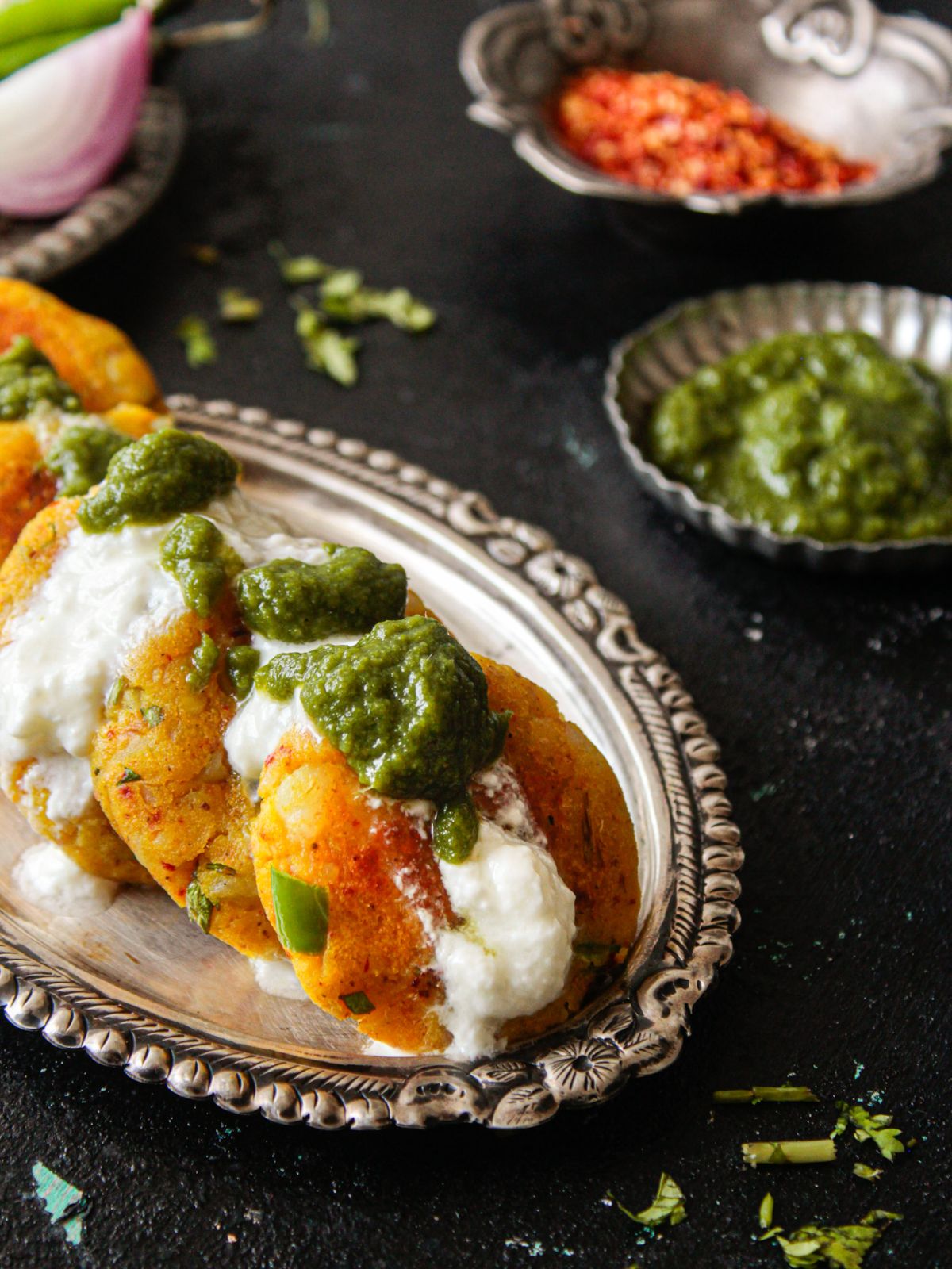 Silver platter of aloo tikki  topped with yogurt and green chutney