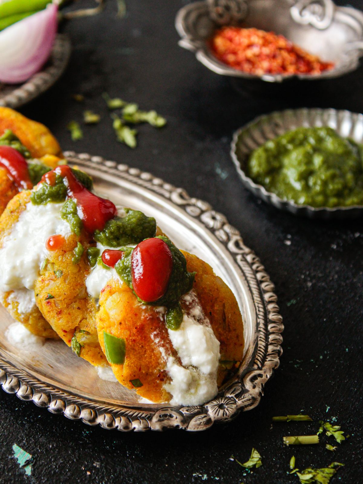 Potato patties on silver platter next to bowl of green chutney