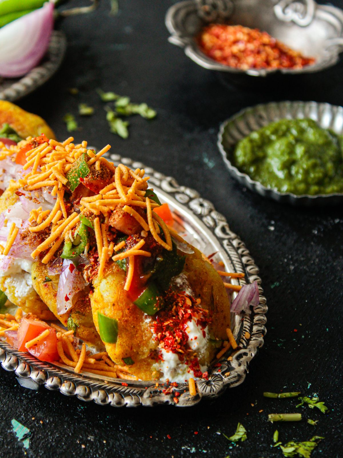 Silver platter topped with aloo tikki chaat on black table