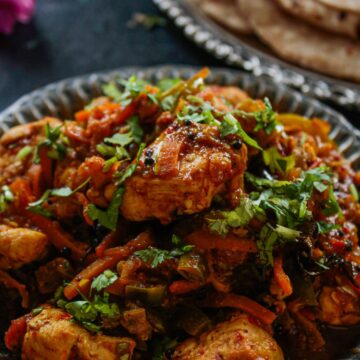 Chicken Jalfrezi in round black plate next to naan
