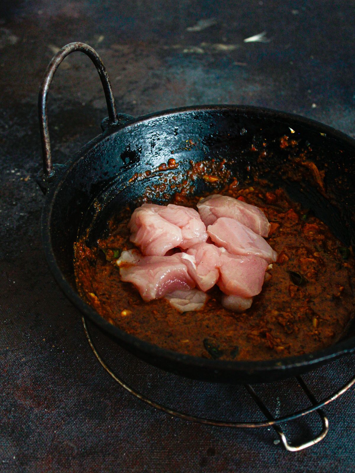 raw chicken being added to curry sauce in wok