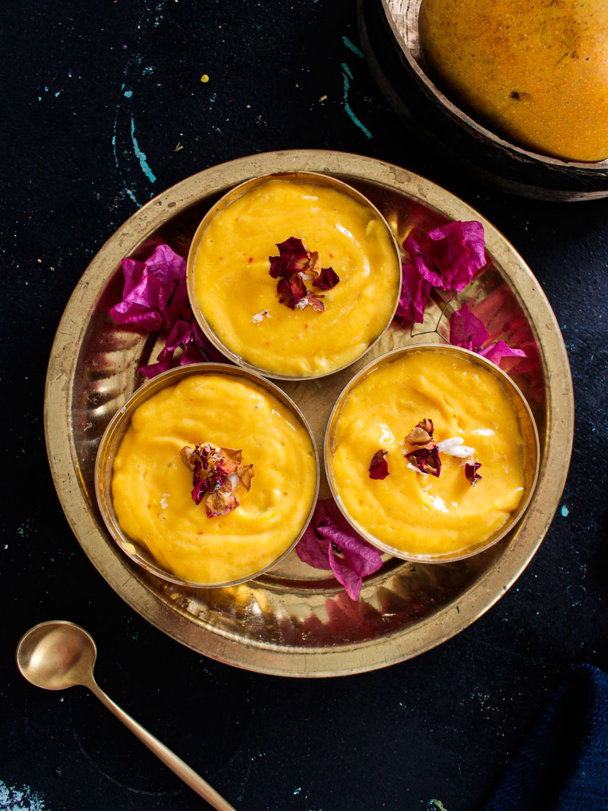 Gold platter filled with bowls of mango shrikhand topped with roses