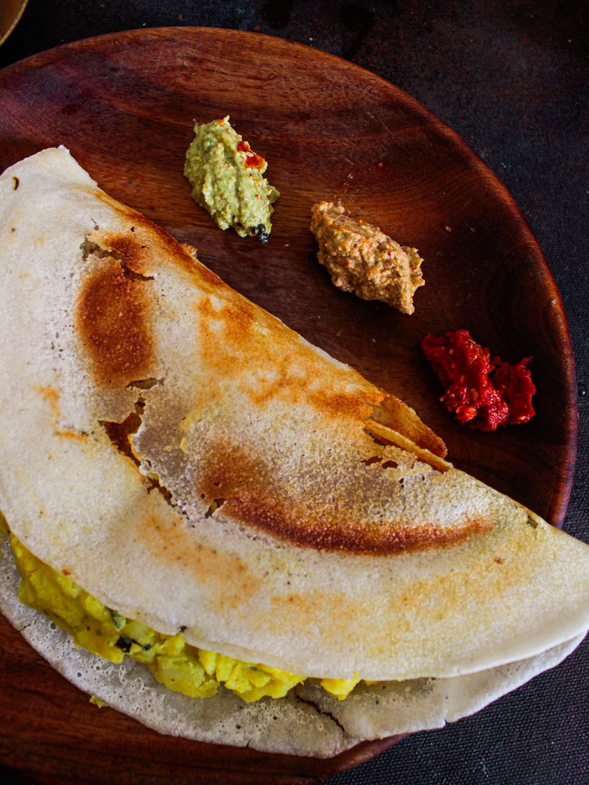 Dosa on wooden plate with chutneys on side