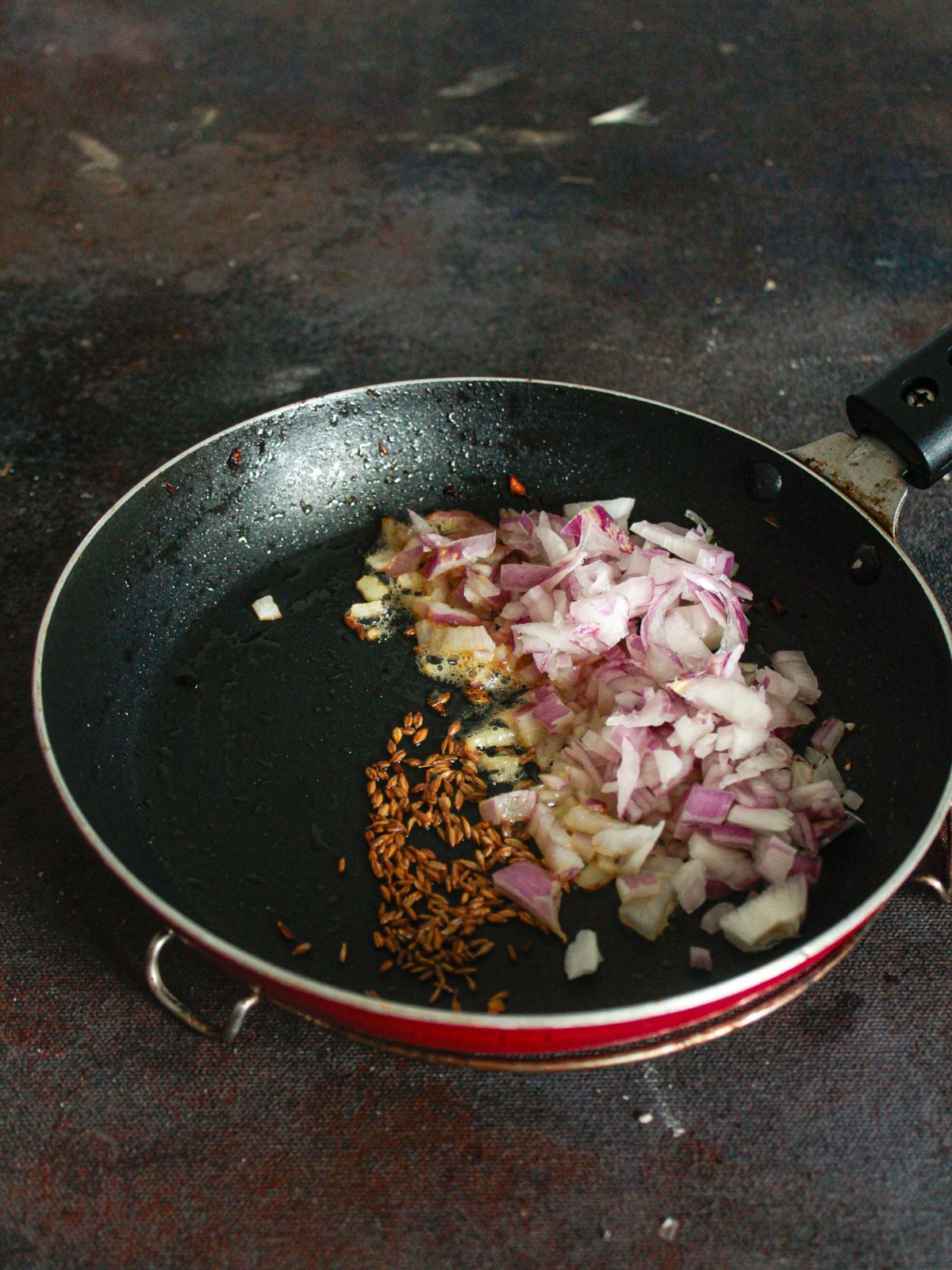 Red skillet with onions and cumin seeds in oil