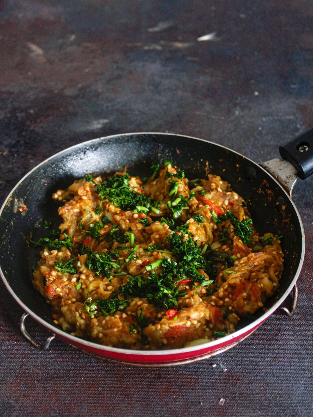 Eggplant mash in skillet topped with coriander leaves