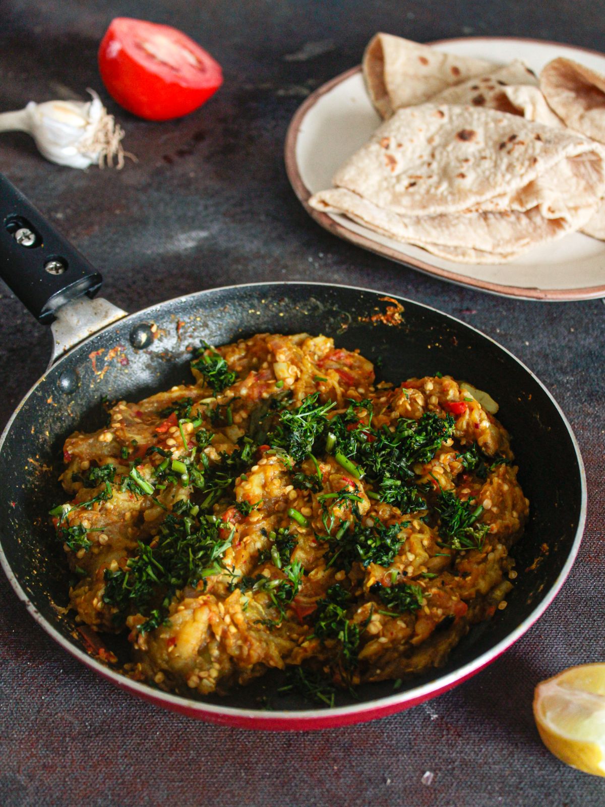 Baingan bharta in skillet topped with coriander next to plate of fresh roti