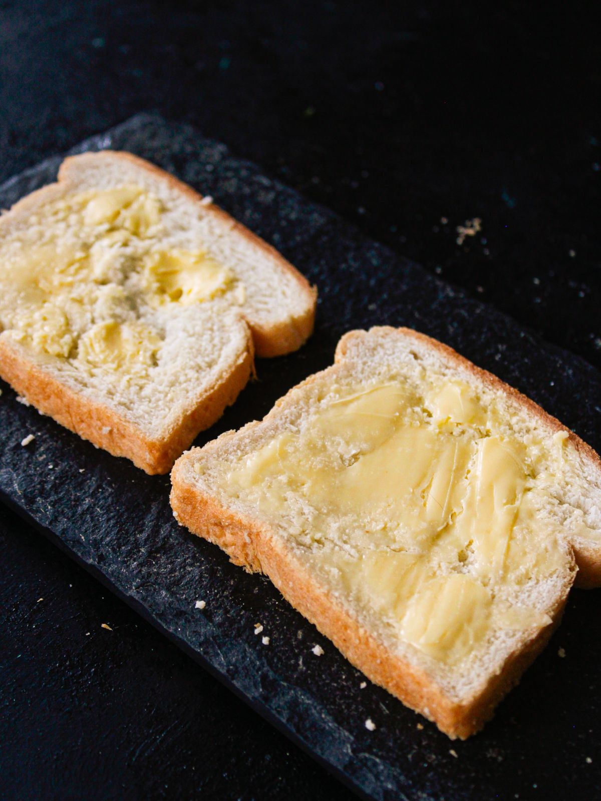two slices white bread with butter on black table