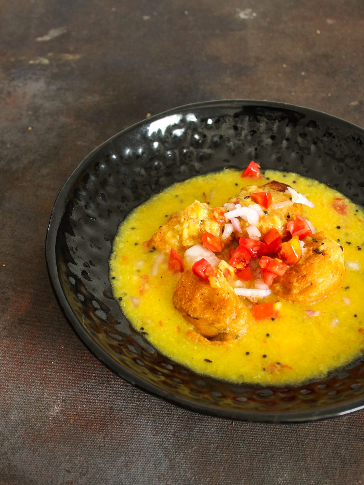 Tomatoes and onions on top of yellow soup with fritters