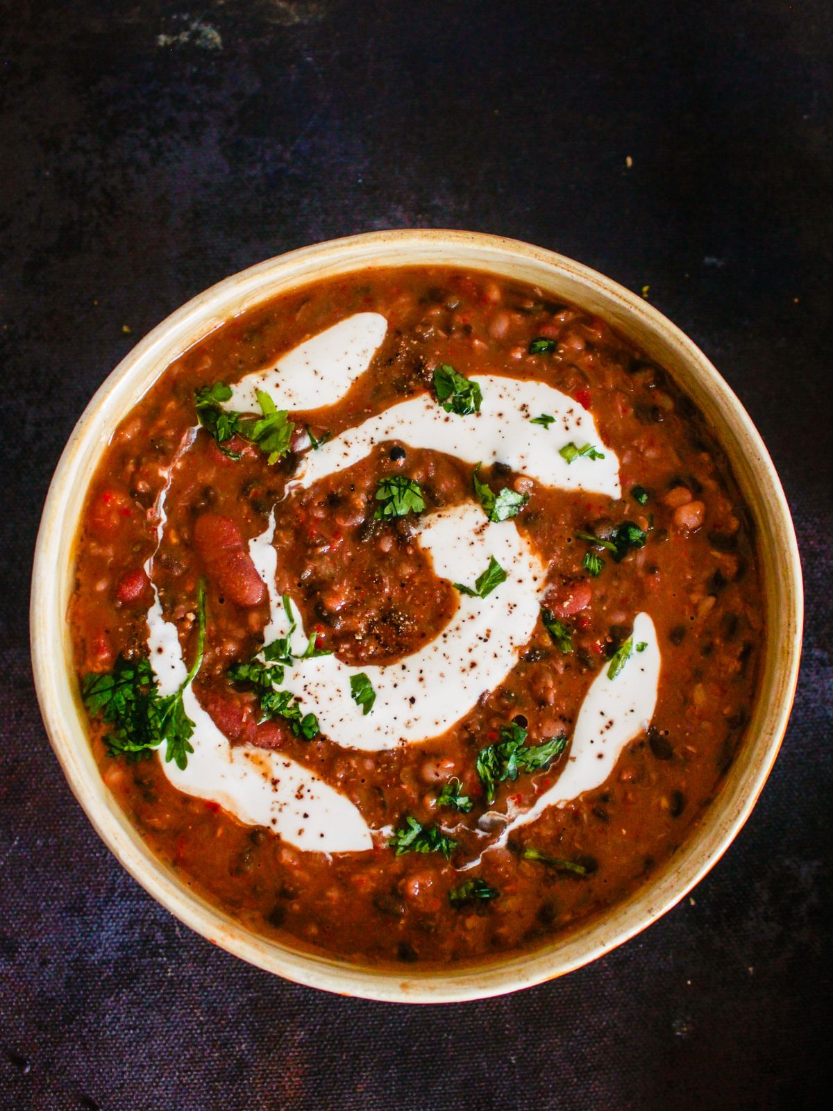 cream bowl of cooked dal makhani with cream on top sitting on black table