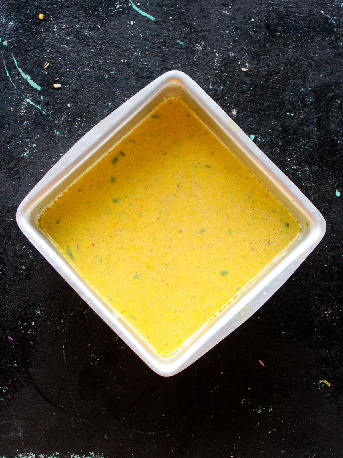 Square white dish filled with yellow batter sitting on black table