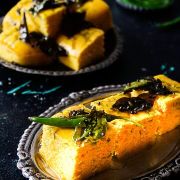 Sliced dhoka on silver platters with green chilies on top