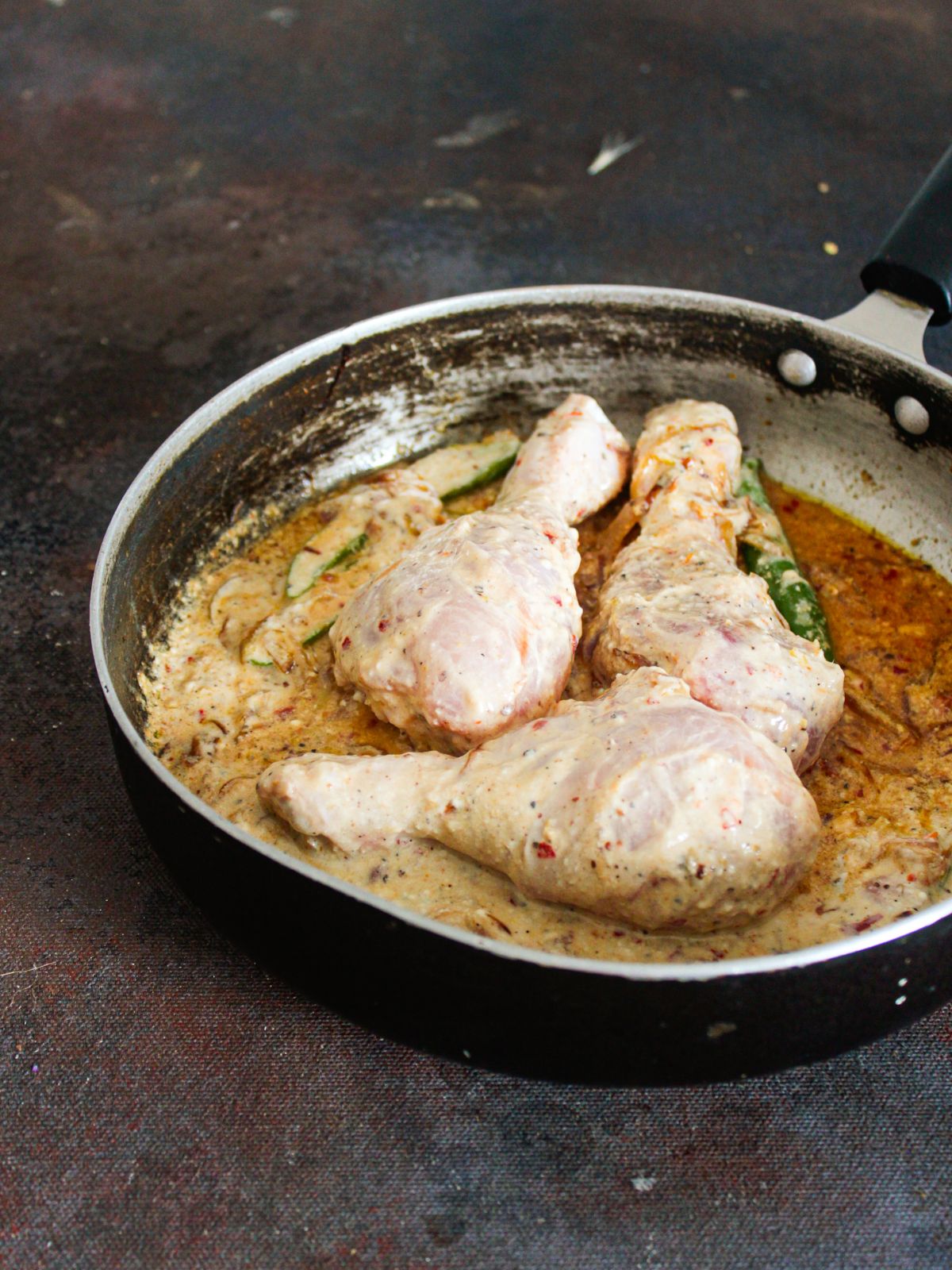 raw chicken legs in sauce in skillet