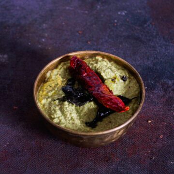 coconut coriander chutney in gold bowl on purple table with red chile on top