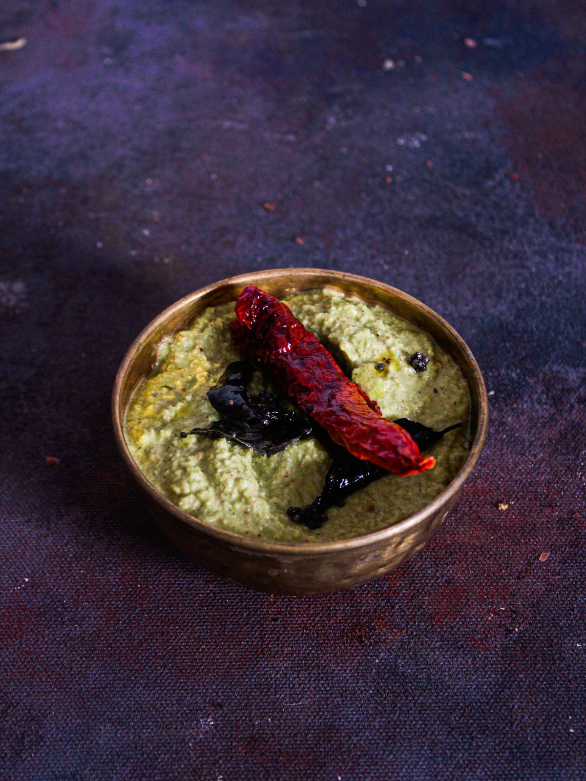 coconut coriander chutney in gold bowl on purple table with red chile on top