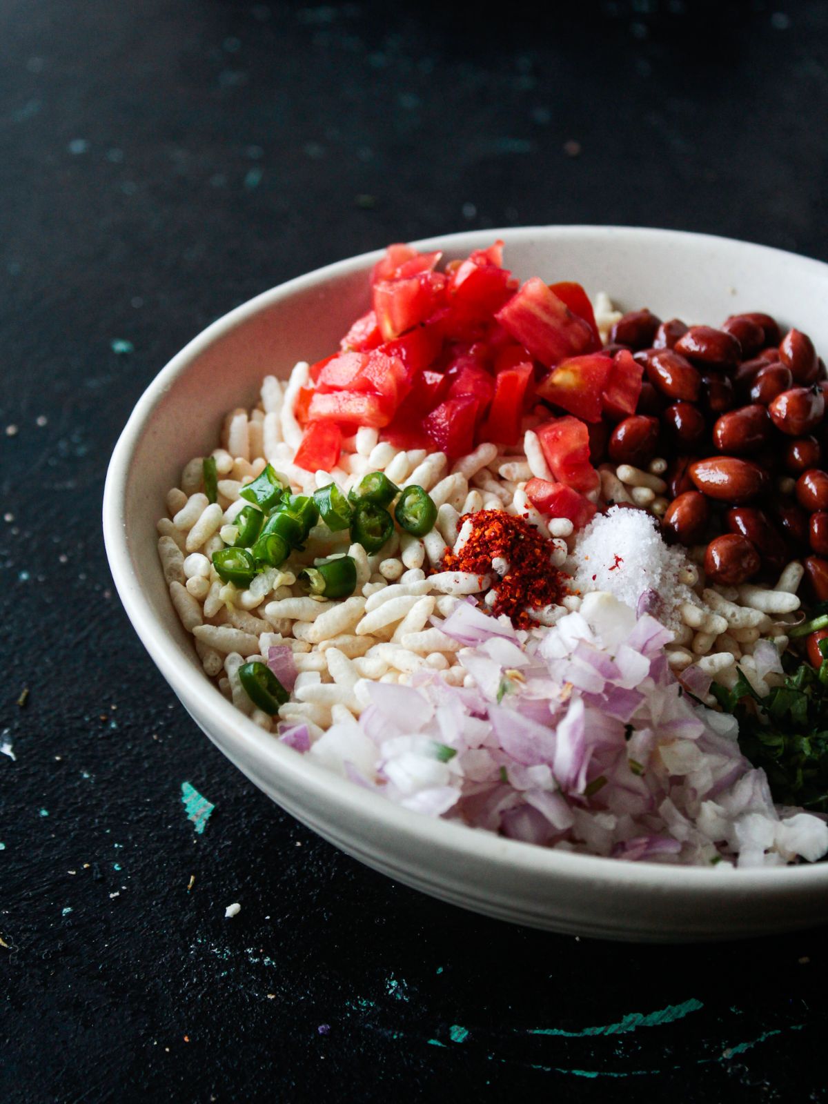 puffed rice, tomato, peanuts, onion, and spices in white bowl on black counter