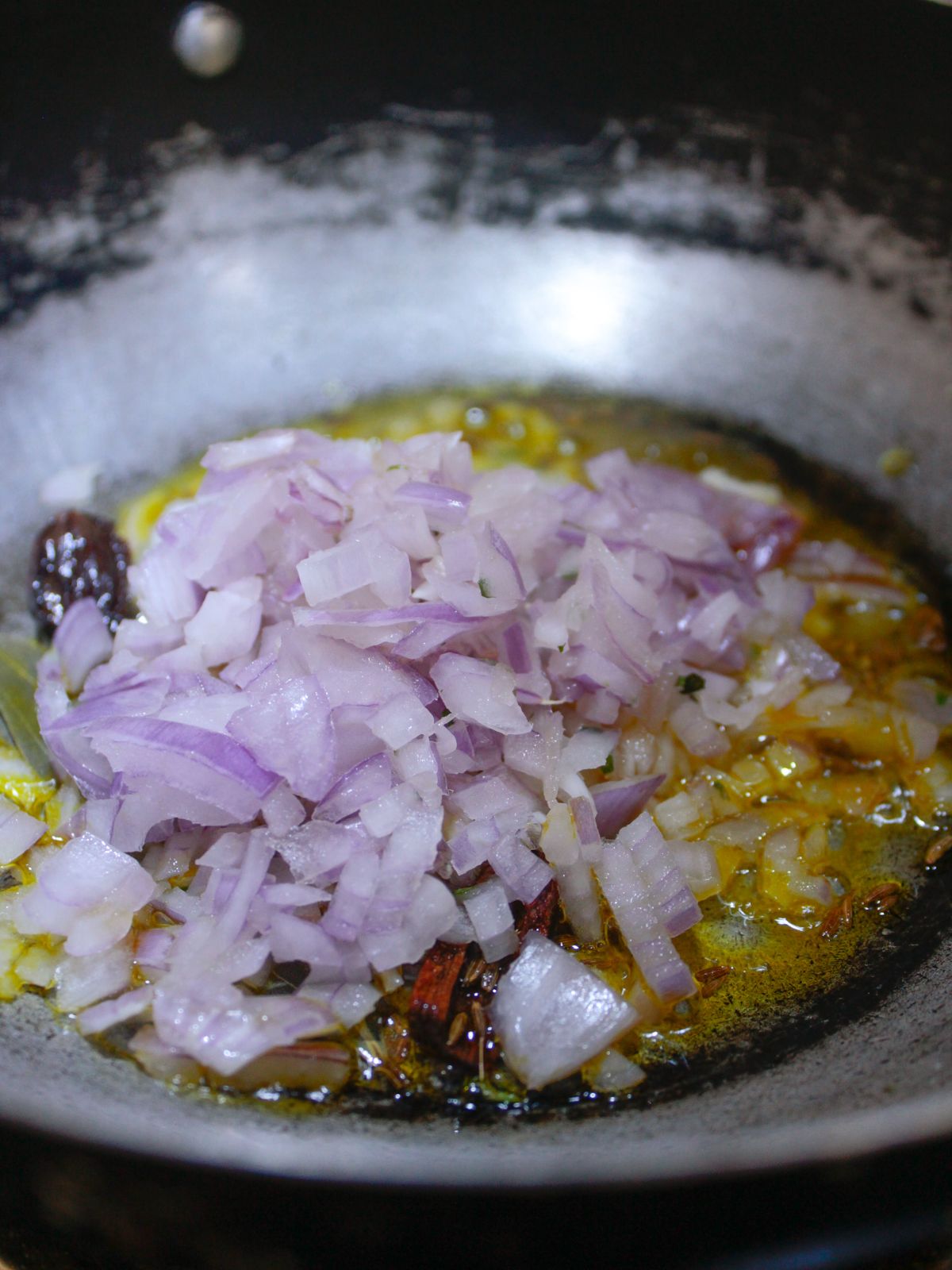 Red onions on top of herbs and oil in skillet