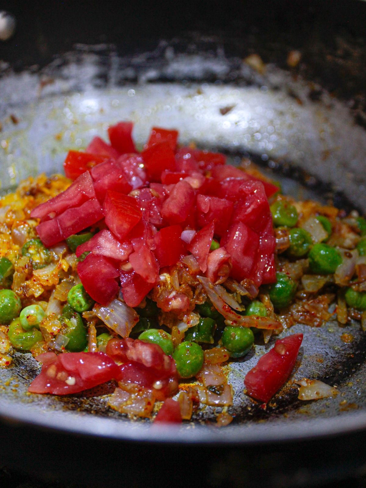 Chopped tomatoes on top of peas and onion in skillet