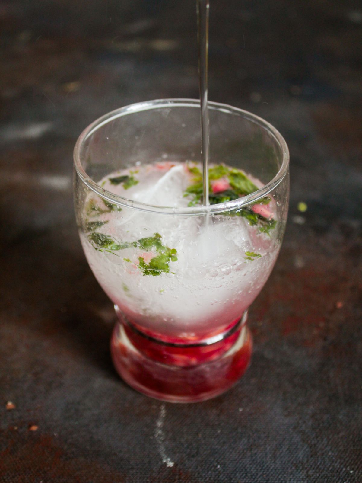 Pouring soda into glass with pomegranates and mint