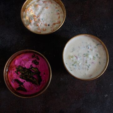 Three gold bowls of raita on black table