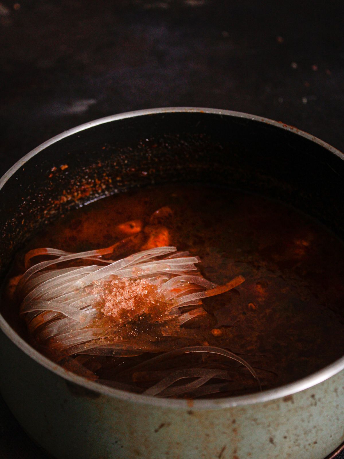 noodles in stockpot with red broth