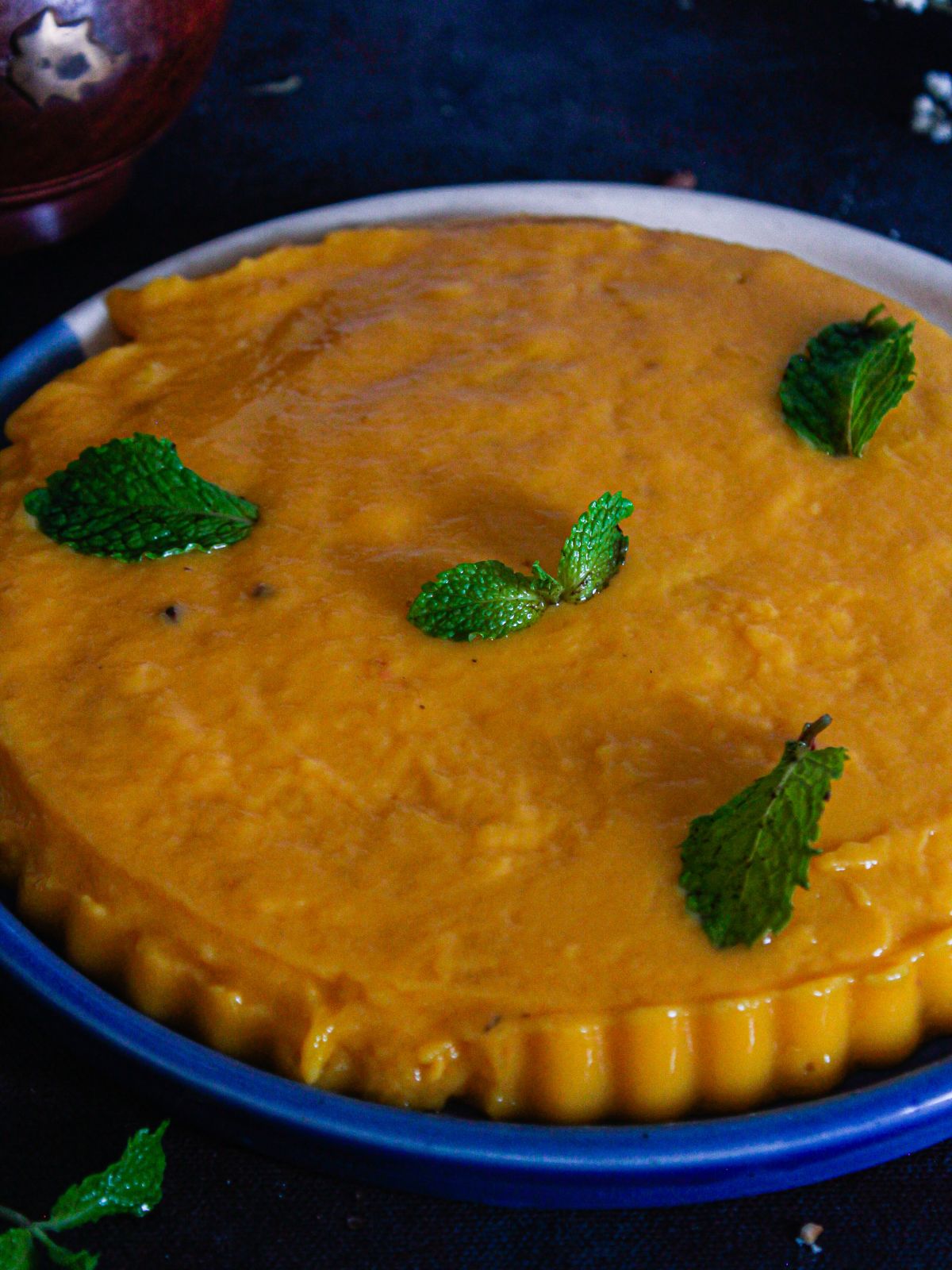 orange mango pudding on blue plate with mint leaves on top