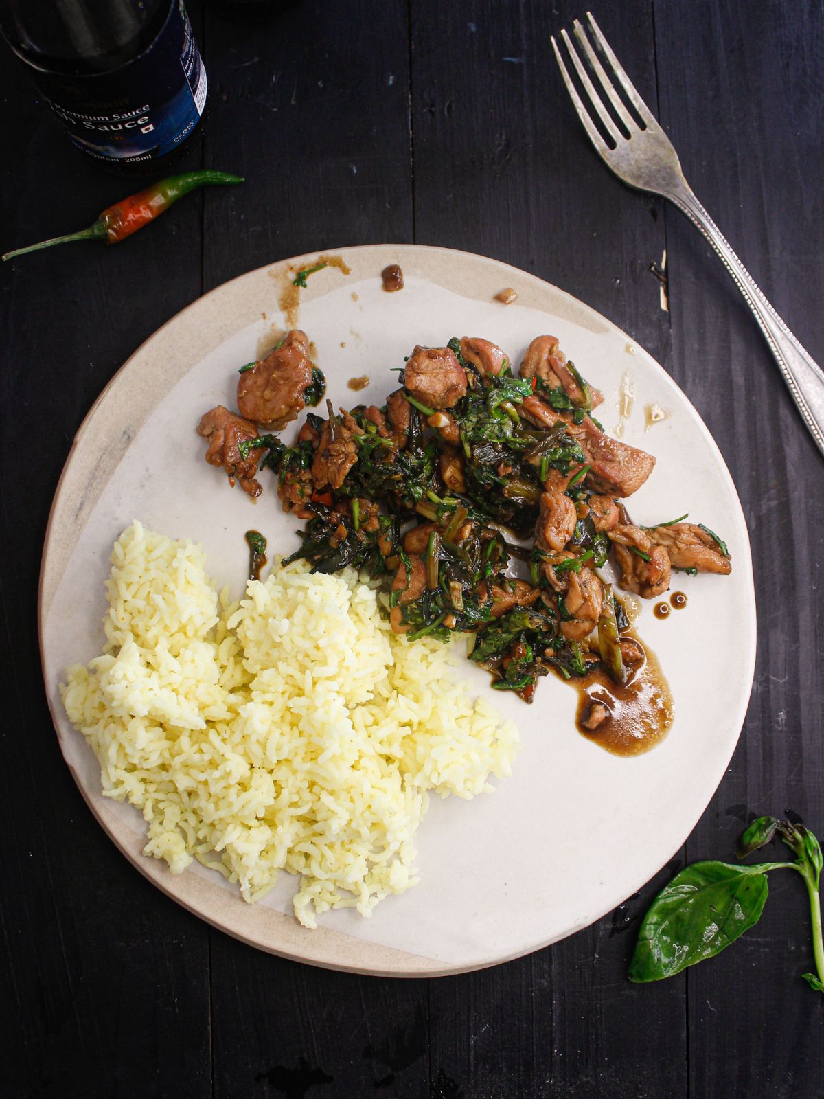 white plate with rice and thai basil chicken on black table