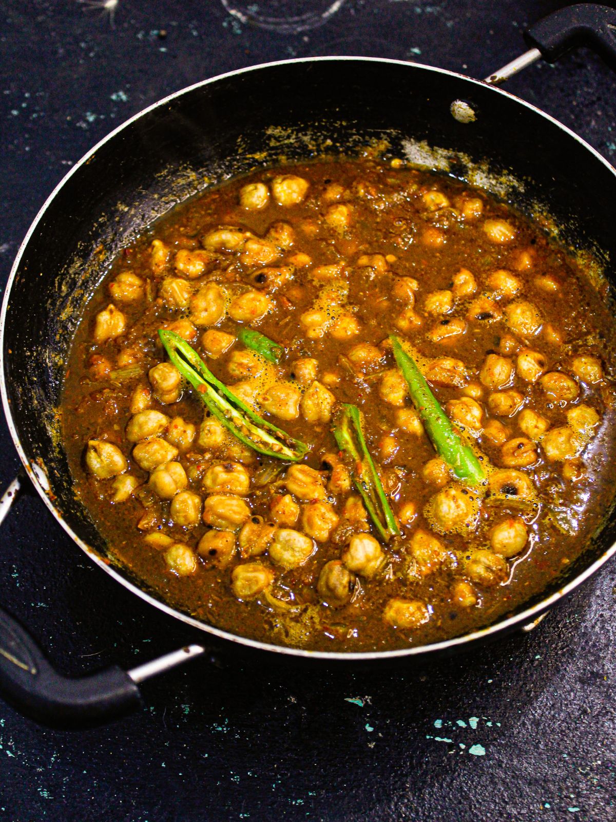 black skillet of chickpea curry with green chile on top